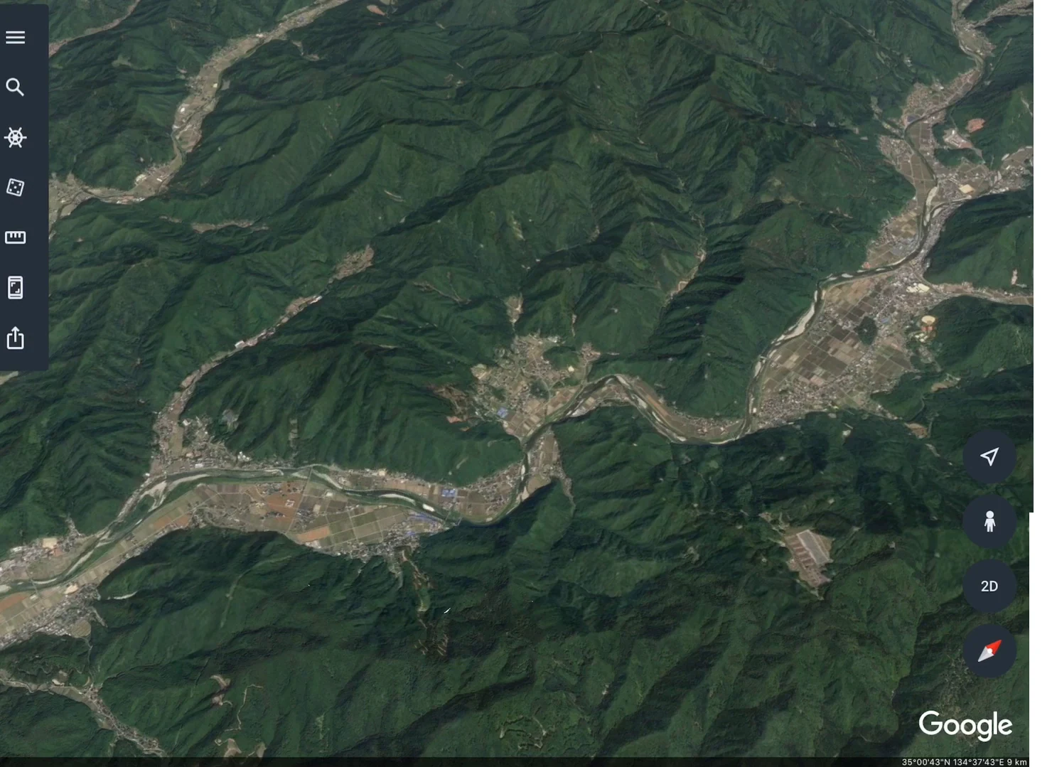 山地の間を蛇行して流れる川と、その両側に広がる谷底平野の航空写真。谷底平野には田畑や集落が並び、周りの山地は森林におおわれている。