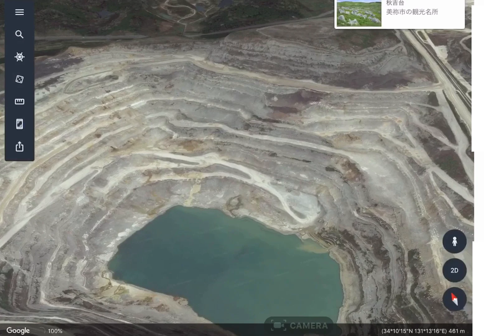 秋吉台の周辺にある石灰岩の採掘場を上空から見た Google Earth の画像。山が階段状に掘り下げられて白っぽい岩肌が広がり、いちばん底には緑色の水がたまっている。右上に「秋吉台 美祢市の観光名所」の表示が写り込んでいる。